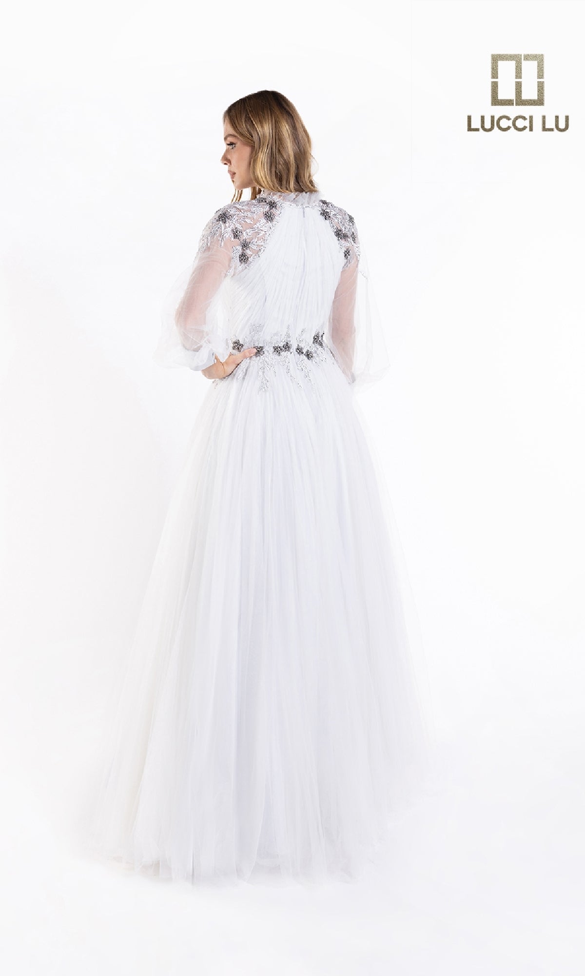 A woman faces away wearing the Lucci Lu C8057, a white long-sleeve formal A-line dress with lace, beads, a sheer sleeve, and fitted bodice. The Lucci Lu logo is in the top right corner.